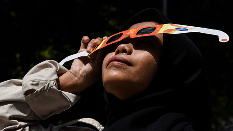 Close up shot of a girl holding up a pair of eclipse glasses