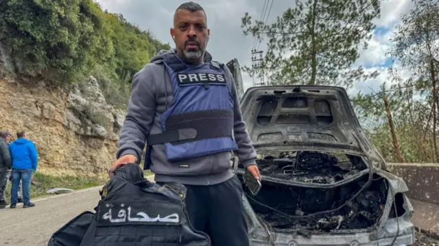 Al Mayadin journalist Jamal Al-Gharabi holds a press vest next to a car destroyed by an Israeli strike that killed Lebanese journalists Al Mayadeen reporter Fatima Ftouni and cameraman Mohammed Ftouni, and Al Manar reporter Ali Shaib, amid escalating hostilities between Israel and Hezbollah