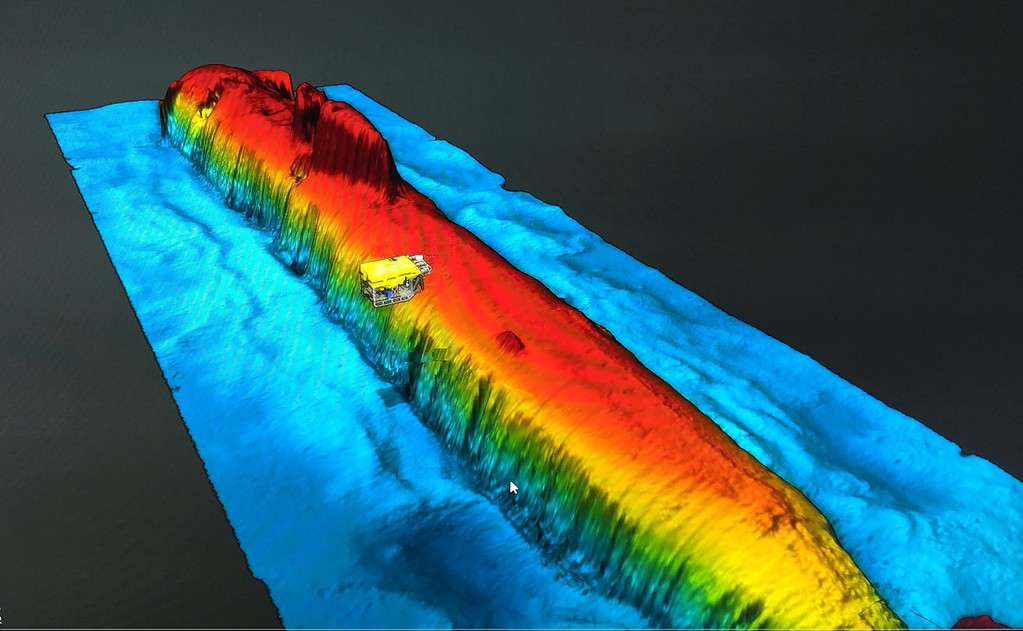 A detailed 3D sonar scan ocean floor showing the sunken Russian nuclear submarine and the ROV operating around it.