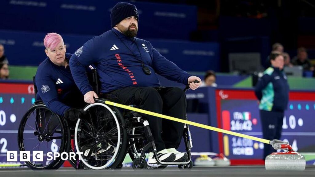 Great Britain's Jason Kean delivers a stone in the wheelchair curling at the Winter Paralympics with Jo Butterfield holding his chair in support
