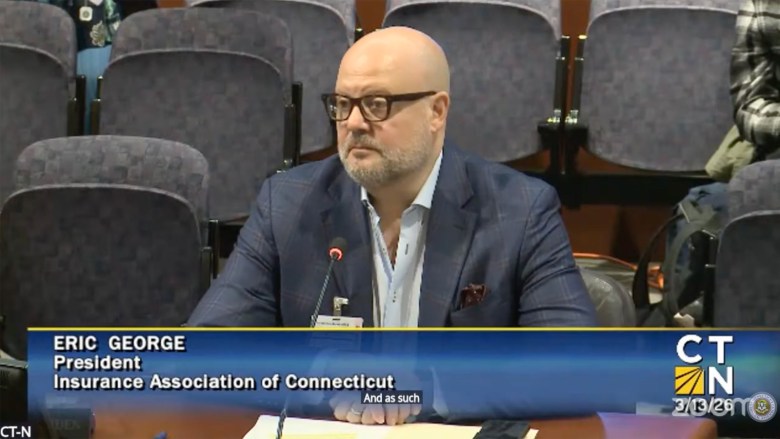 Man pauses during comments into a microphone with empty seats in the back