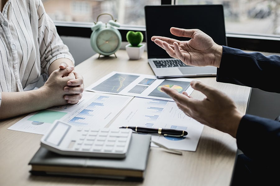 Two people having a discussion about finances at a desk full of calculators and spreadsheets