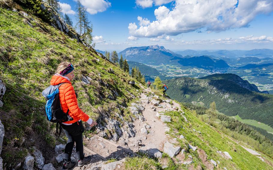 A woman hikes a trail along the side of a mountain on a lightly cloudy day.