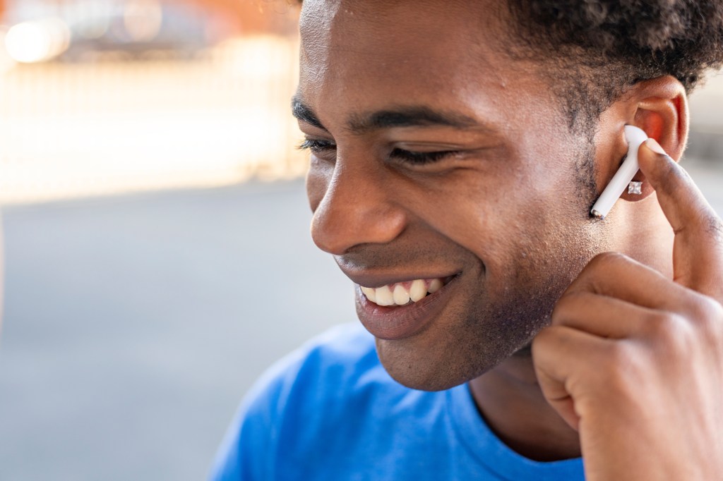 A happy African American man wearing wireless earbuds and a blue shirt smiles.