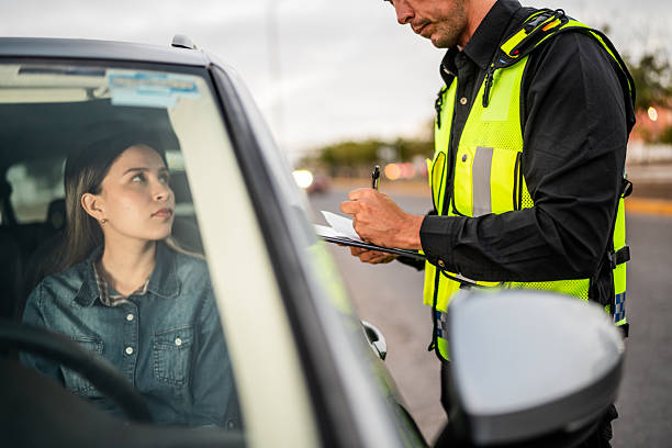 Traffic officer in a reflective vest writes on a clipboard while a driver sits in a car during a roadside stop.