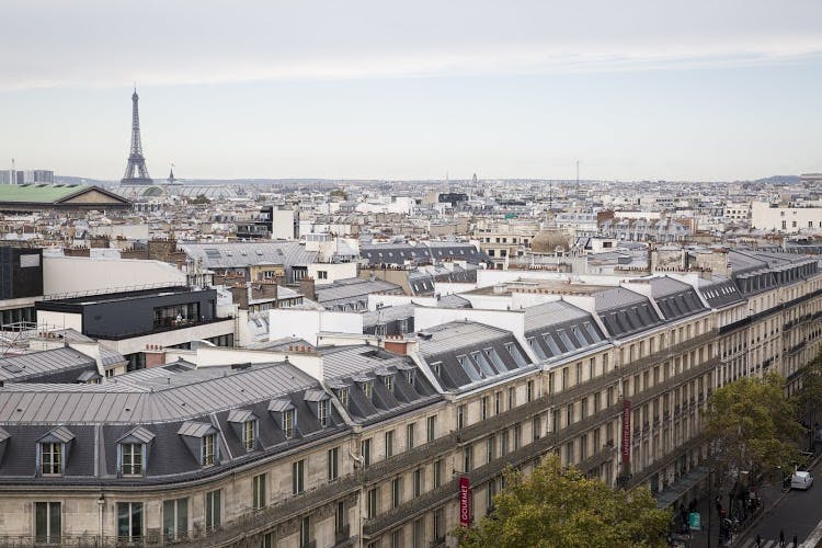 Paris cityscape with rows of classic rooftops and the Eiffel Tower visible in the distance under a gray sky.
