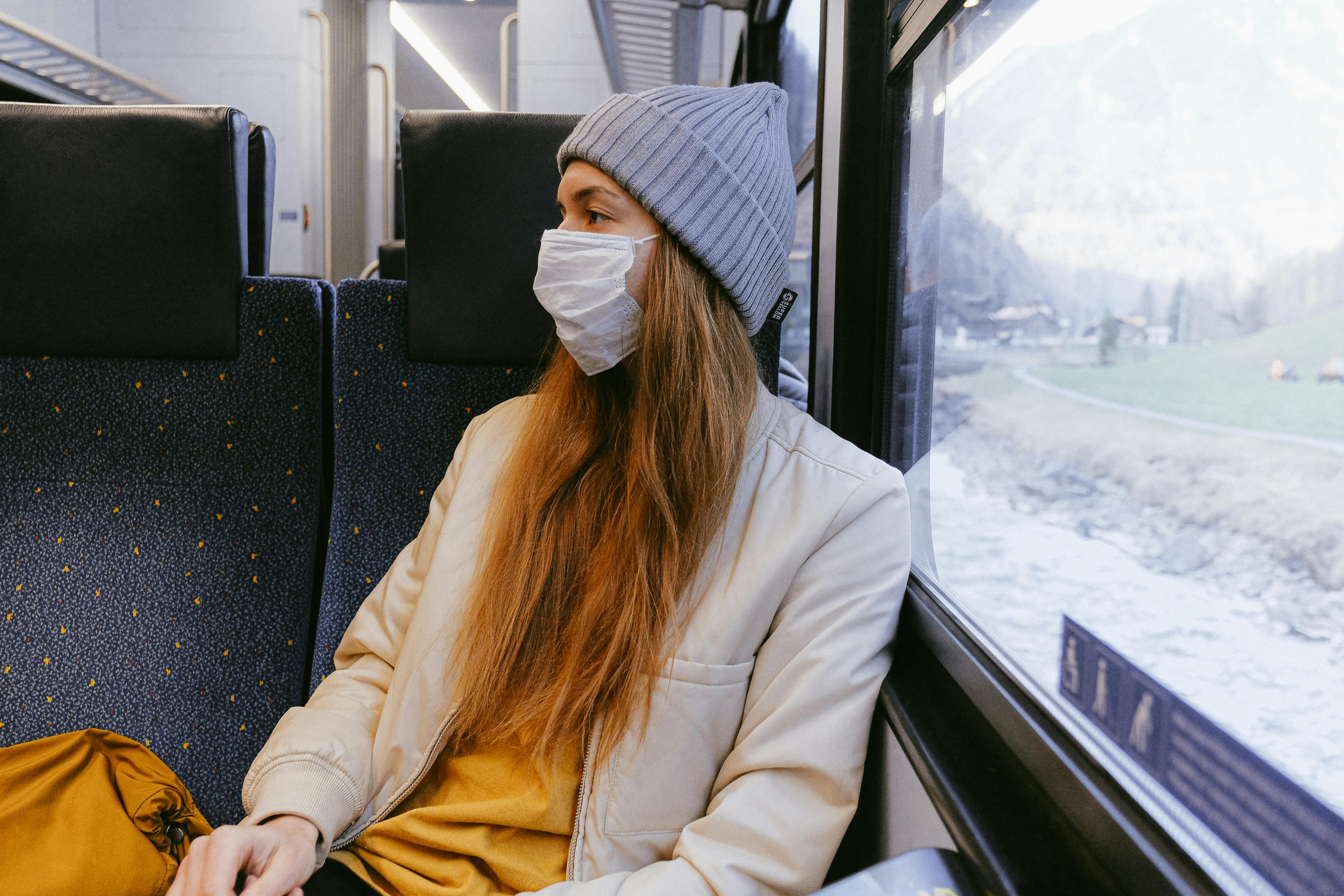 Woman wearing a face mask sits by a train window, looking outside during travel.