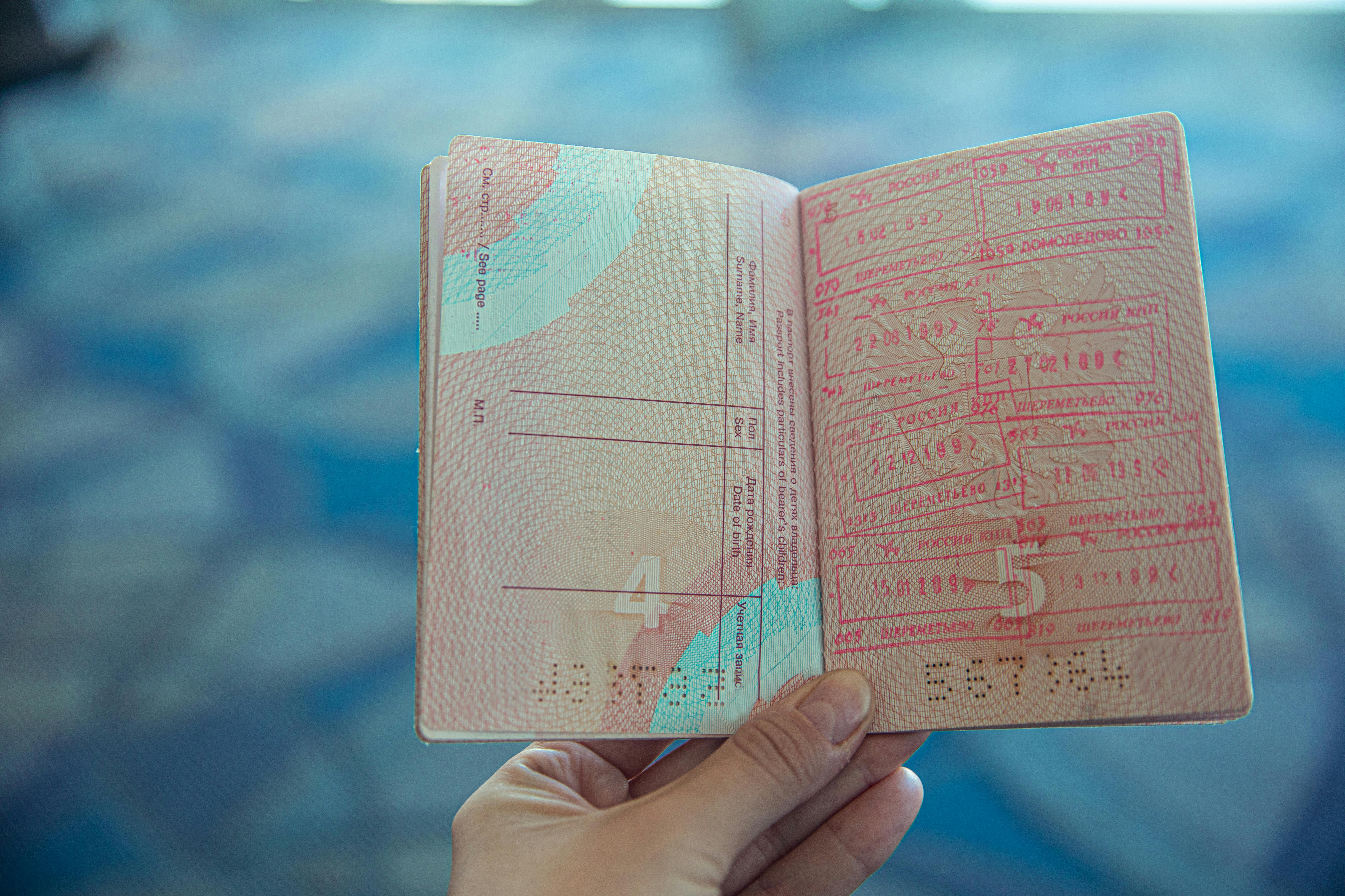 Hand holding an open passport with multiple entry and exit stamps on the pages.