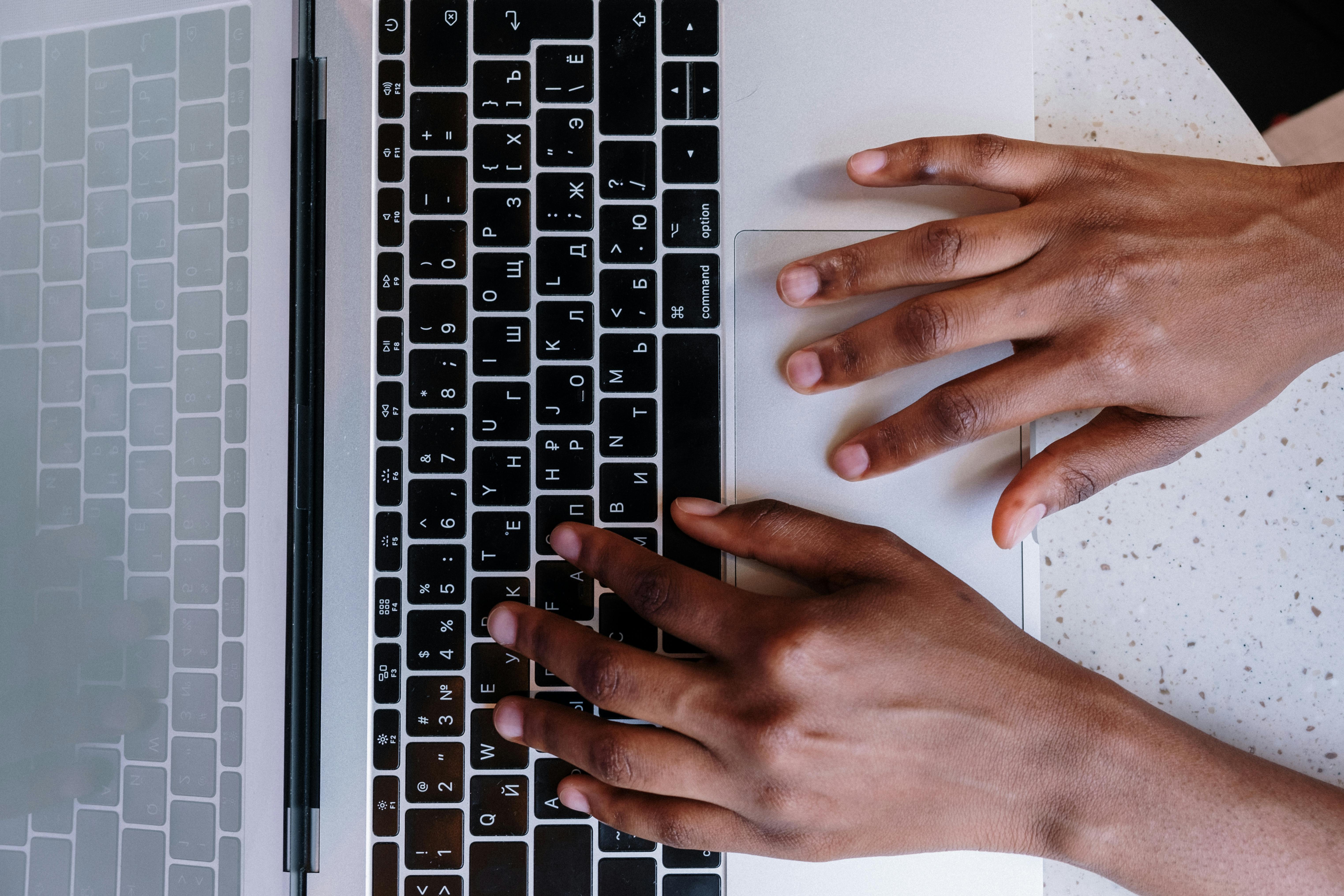 Top view of hands typing on a laptop keyboard on a desk.