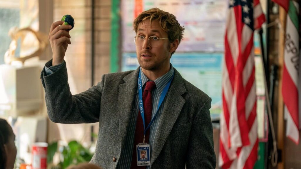 Production still from Project Hail Mary showing Ryan Gosling in a suit and glasses in a classroom holding up a mini Earth.