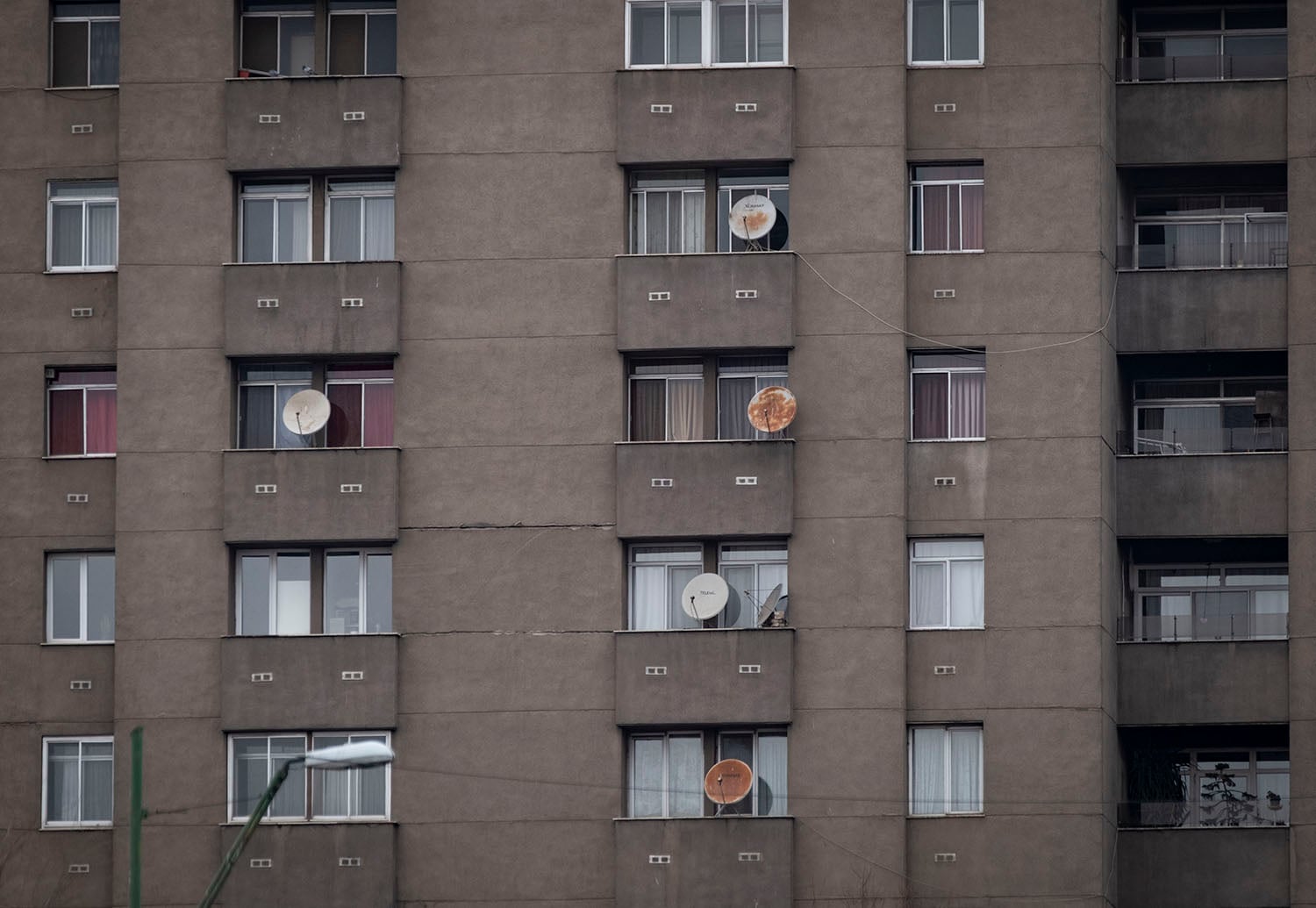 An apartment building of at least six stories high with several old satellite dishes set up on narrow balconies in front of exterior windows.