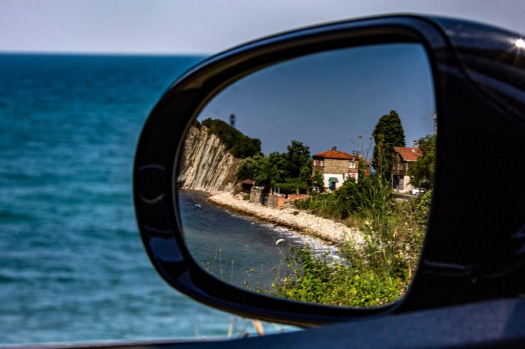 A coastal village near Kiyikoy reflected in a car’s side mirror, with the Black Sea and rocky cliffs in the background. (Adobe Stock Photo)