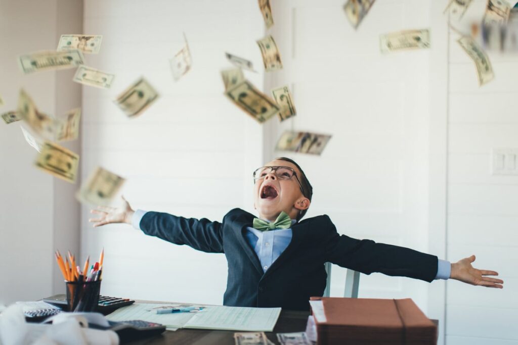 A boy sitting at a desk as money falls around him