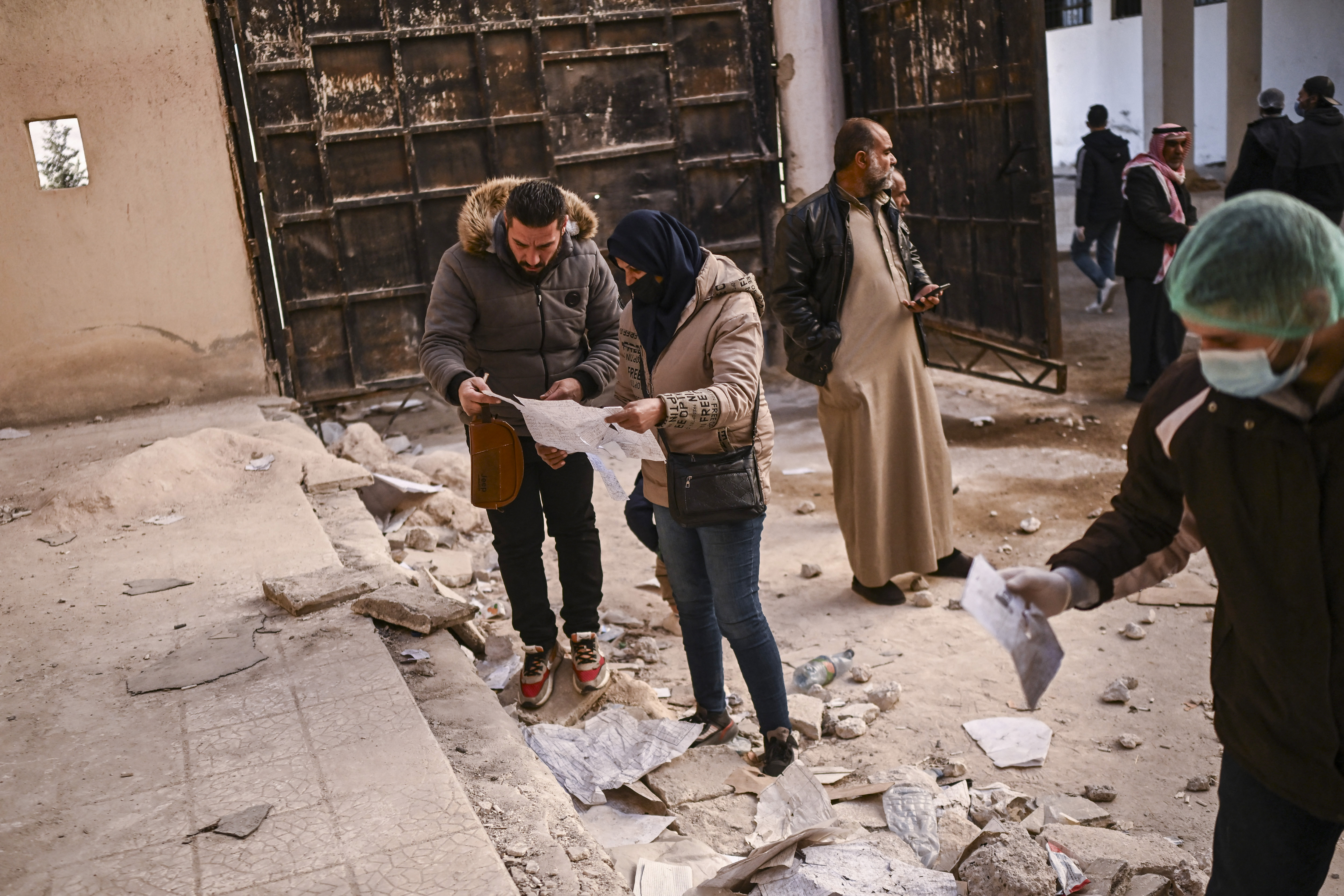 People look at damaged documents as they search for missing relatives at the Saydnaya prison, north of the Syrian capital Damascus, on December 15, 2024. The dramatic liberation of Saydnaya prisoners came hours after Islamist group Hayat Tahrir al-Sham and allies took the nearby capital on December 8, having sent ousted president Bashar al-Assad fleeing after more than 13 years of civil war. (Photo by Aris MESSINIS / AFP)
