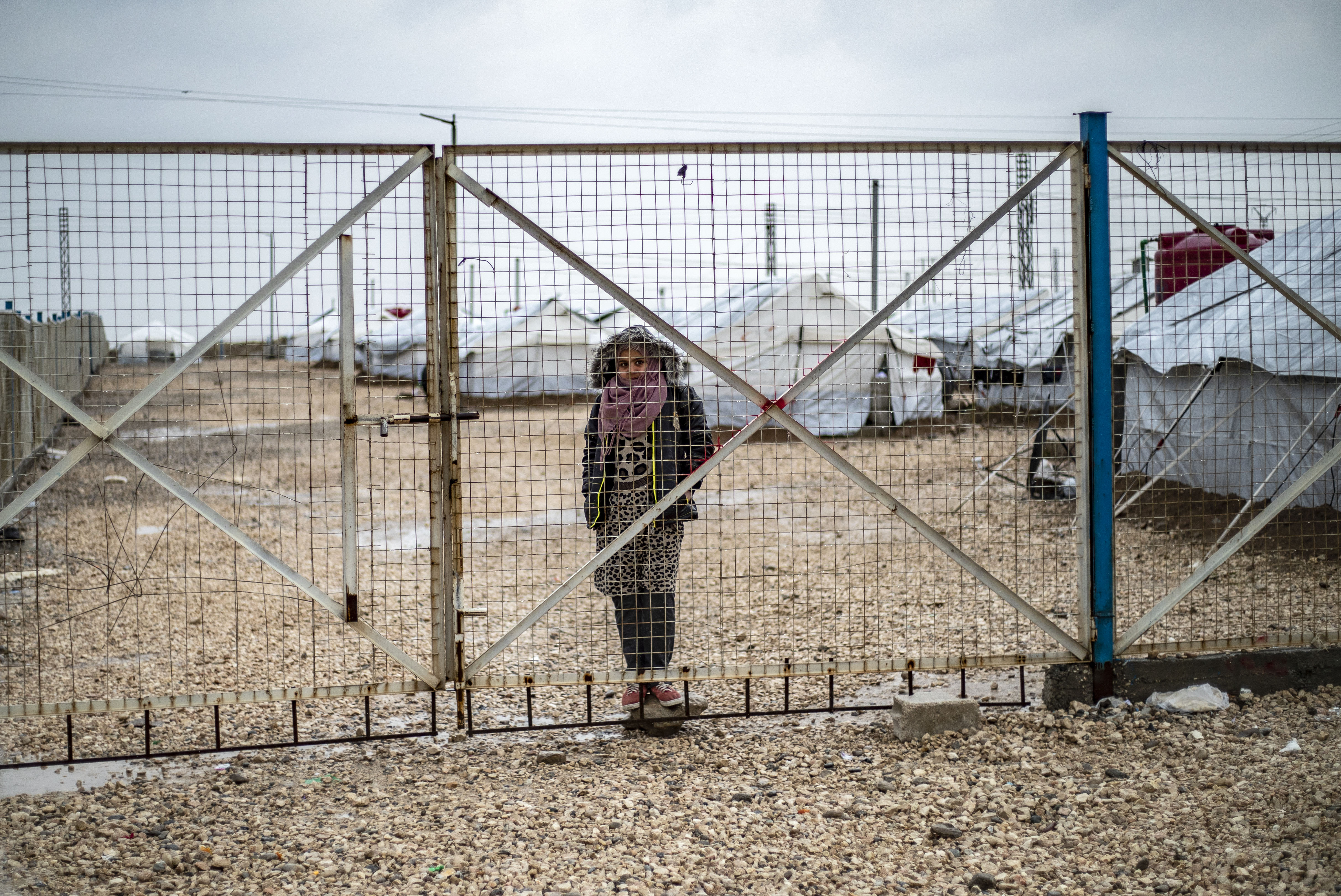 A youth looks out through a metal fence as she stands in the rain at Camp Roj in Syria's northeastern Hasakah province.