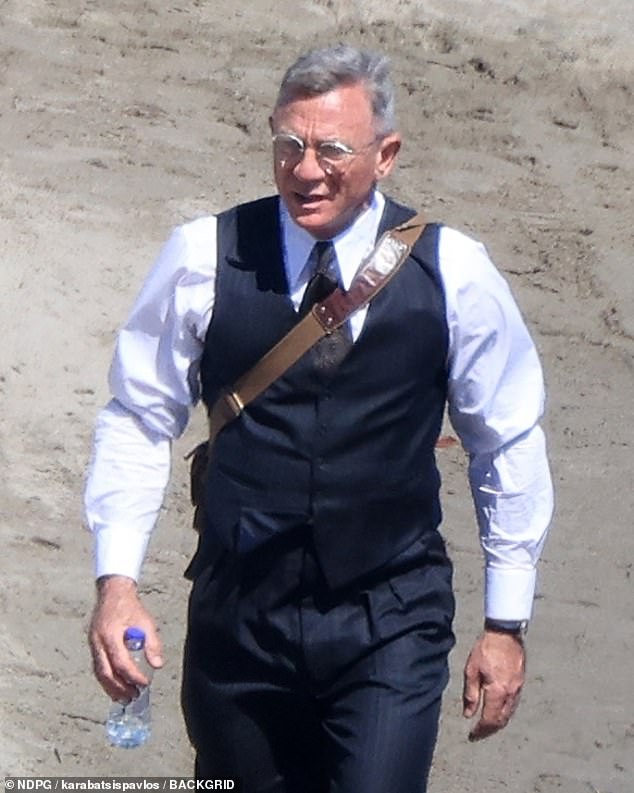 Daniel also carried a brown leather shoulder bag and a bottle of water as he strolled along the beach