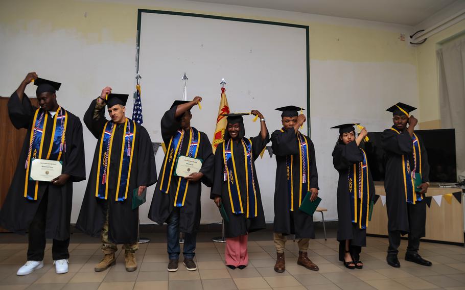 Seven soldiers in graduation caps and gowns wearing Army stoles turn their tassels during a ceremony in Powidz, Poland.