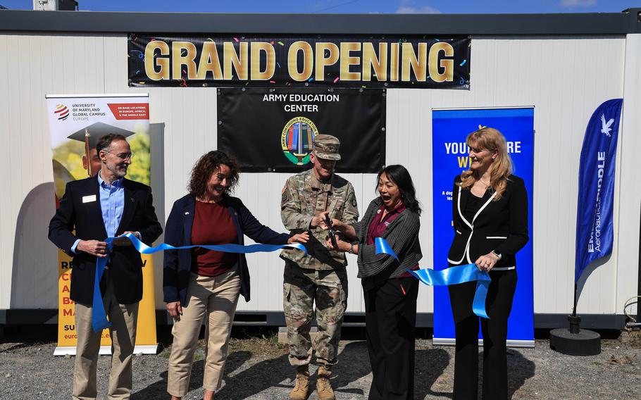 Military and civilian officials cut a blue ribbon in front of a Grand Opening banner for the new Army Education Center in Powidz, Poland.
