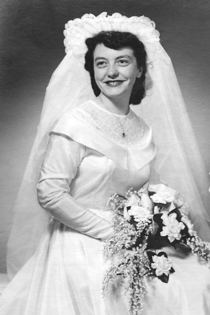 An black and white photograph of a woman smiling in a wedding dress and a veilwhile holding a bouquet.