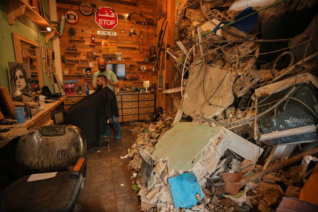Barber Mohammad Mehdi cuts the hair of his client Ayman Al Zein inside his shop, which was damaged in an Israeli airstrike that also damaged Al Zein's shop, in Dahiyeh, Beirut's southern suburbs, Lebanon, Saturday, April 18, 2026.