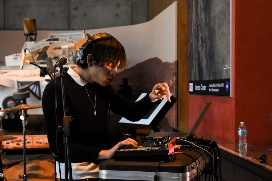 Man wearing black and white and headphones performs music on a synthesizer