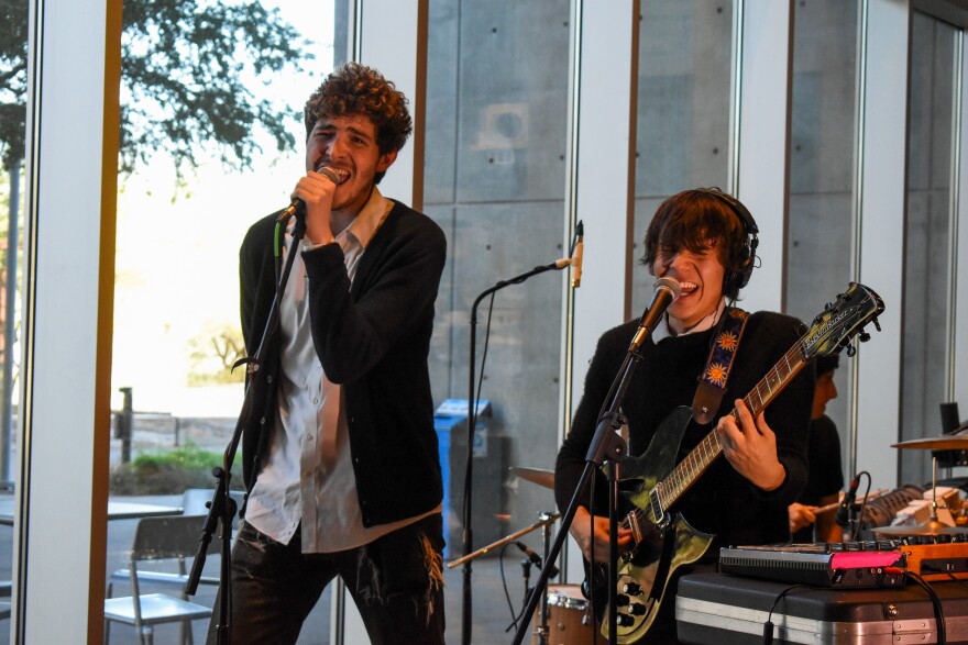 Man sings into microphone while second man plays guitar and sings into separate microphone