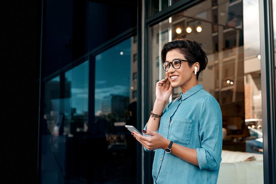 Woman stands outside and puts her earpods in to listen an AI-focused podcast about business