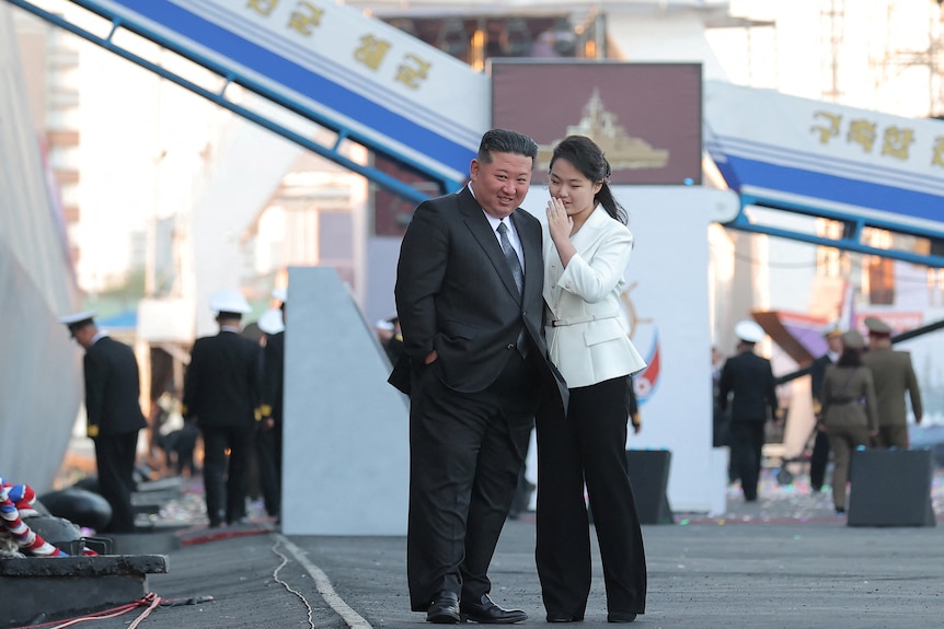 A girl whispers into a man's ear with a big ship in the background.