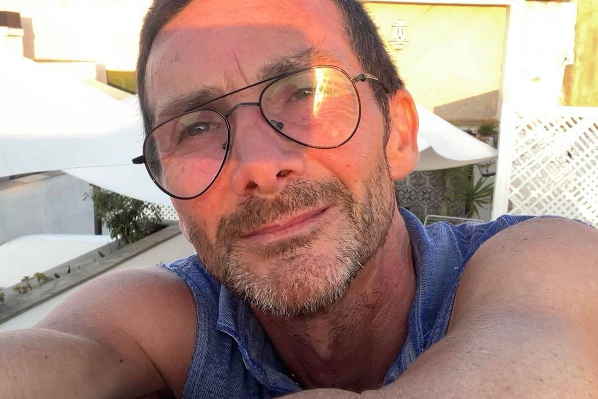 An individual wearing glasses and a blue sleeveless top is smiling and posing for a photograph against a backdrop that includes 