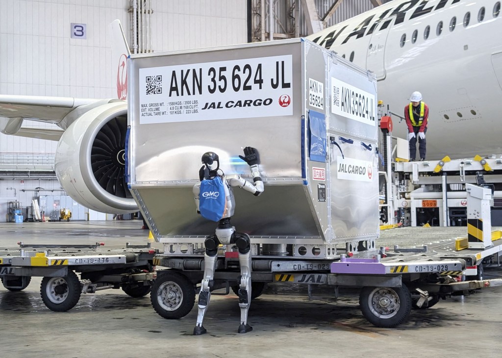 A humanoid robot pushes a cargo container during a media demonstration inside Japan Airlines's airplane hangar at Haneda airport.