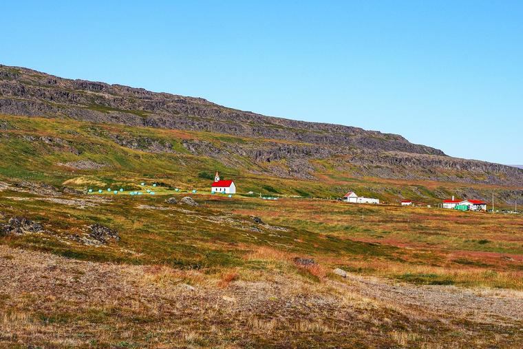 A Catholic chapel stands on a mountainside in Vatnsfjörður (Vatnsfjarðarkirkja), in Iceland’s Westfjords, under a clear summer sky.