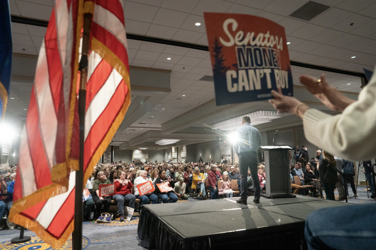 Graham Platner is seen from behind while standing on a temporary stage in front of a large audience.