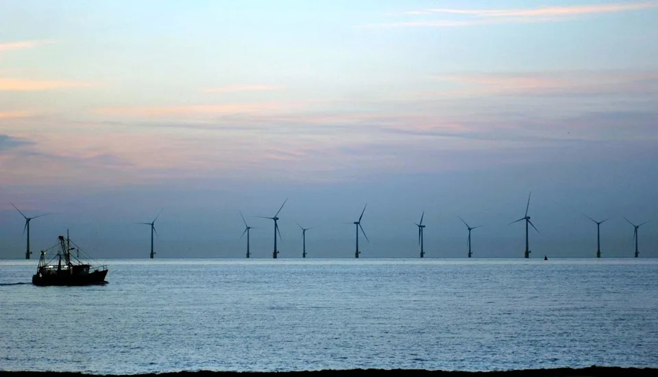 Dawn breaks at Caister-on-Sea looking out towards a large windfarm as a fishing boat passes by 