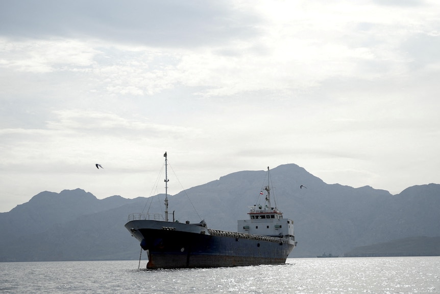 A large tanker sits on the ocean against a mountainous landscape.