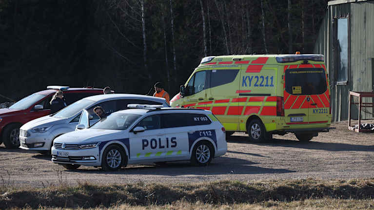 Police and rescue vehicles parked on a gravel road next to a shed, with trees in the background.