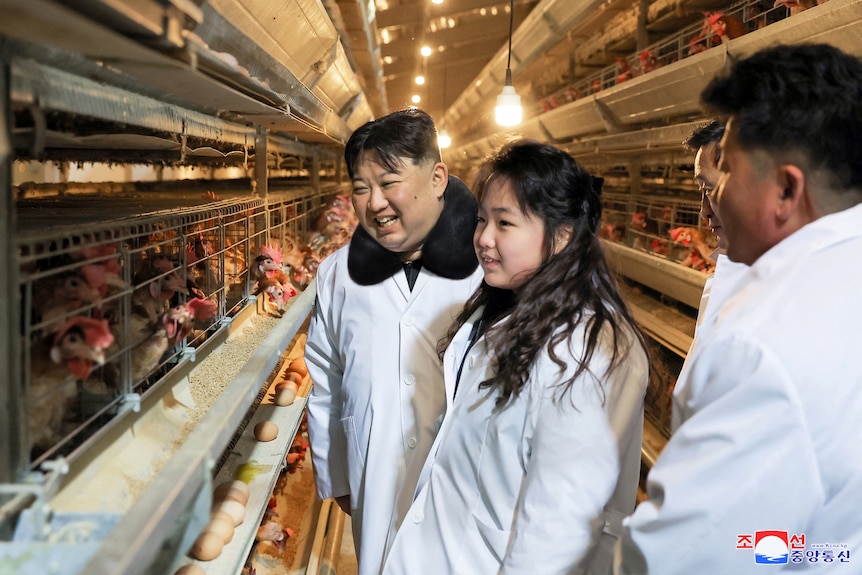 A man and girl wear white lab coats among chickens in cages.