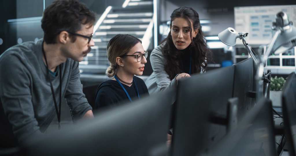 Microsoft taps Anthropic’s Mythos to strengthen secure software development Team of Three Talented Young Software Engineers Use Computer to Discuss a Technological Project in Modern Industrial Office. Group of Male and Female Scientists Work in Research and Development Center
