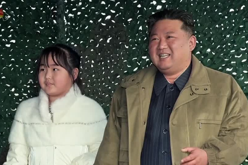 Kim Jong Un wearing a black shirt and jacket stands next to his daughter in a white coat.