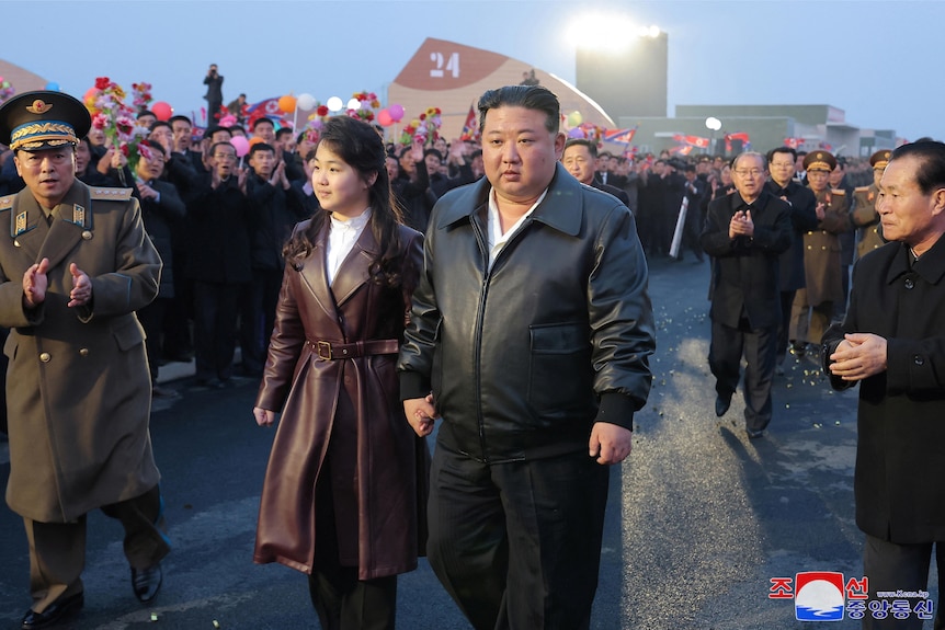  A girl and man walk hand in hand as people cheer them on.