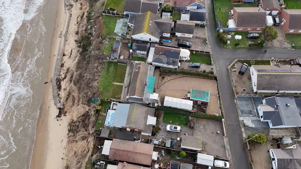 An aerial view of a number of chalets and properties on the edge of a cliff, with the sea below. 
