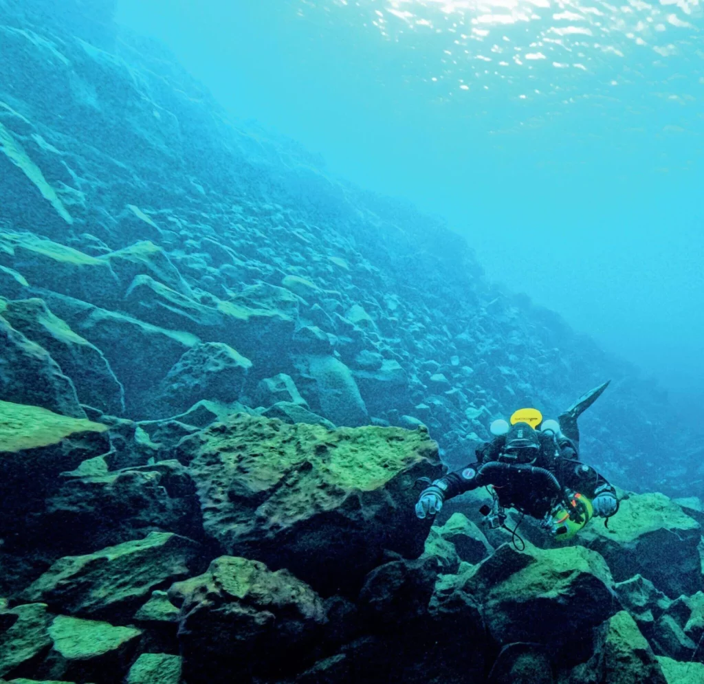 Scuba divers descending into the luminous blue water of the Silfra fissure between the North American and Eurasian tectonic plates.