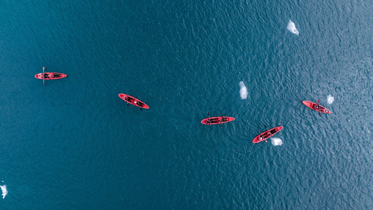 A sea kayak floating in the icy blue waters of Svalbard, Norway, near a rocky coastline