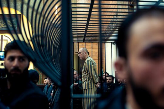 First transitional justice trial in Syria. Photo: Atef Najib (a former senior official in Bashar al-Assad’s regime), wearing a striped prison uniform and with a shaved head, stands in the dock behind bars.