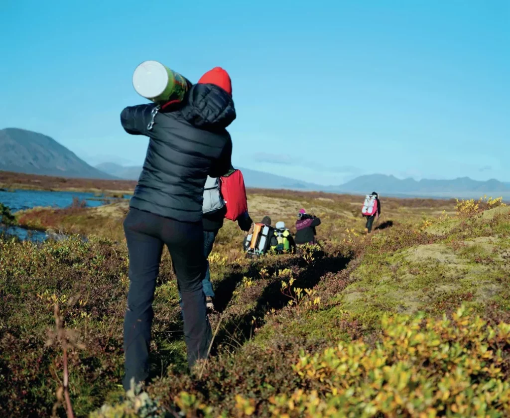 Expedition members transporting heavy technical diving equipment and rebreathers across Icelandic volcanic terrain.