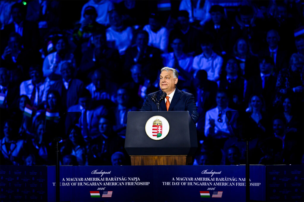 Hungary's Prime Minister Viktor Orban speaking at a podium during a pre-election rally in Budapest, Hungary, with his supporters seated behind him lit in a dark blue light.