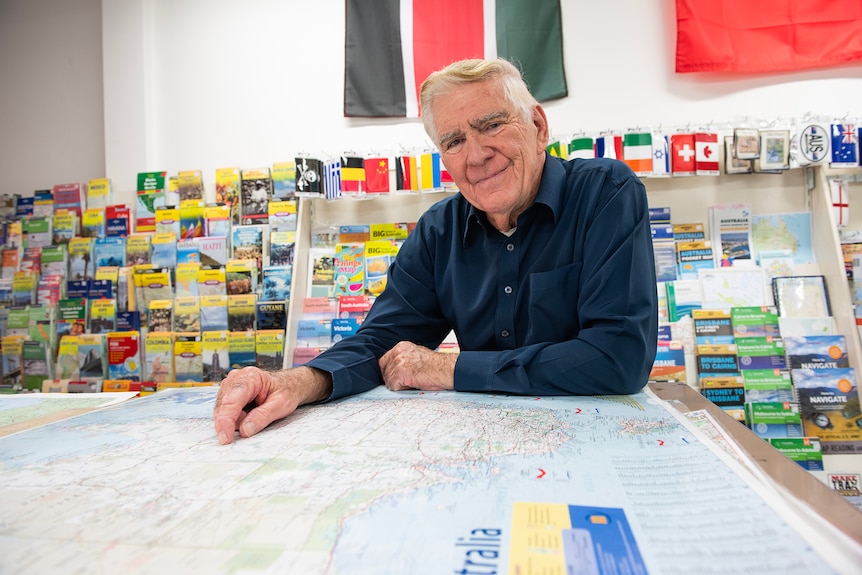 A man leaning over a large map with rows of folded maps behind him.