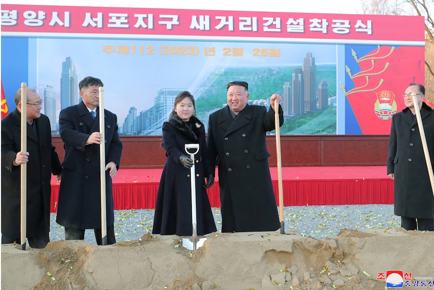 A girl and several men hold spades as they smile for the camera.