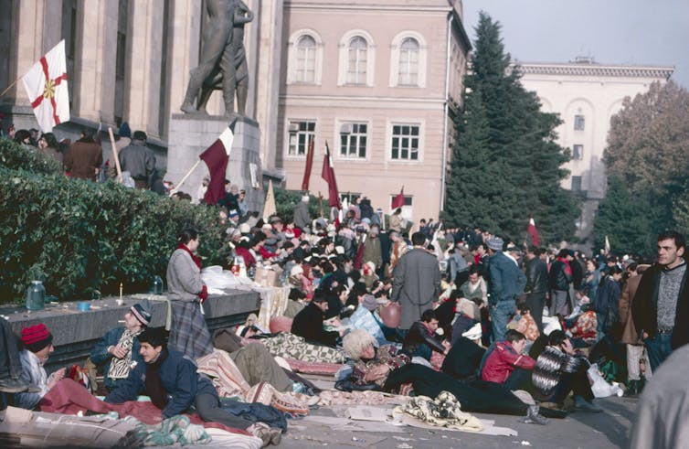 People engaged in a hunger strike lie on a pavement outside a parliamentary buidling.