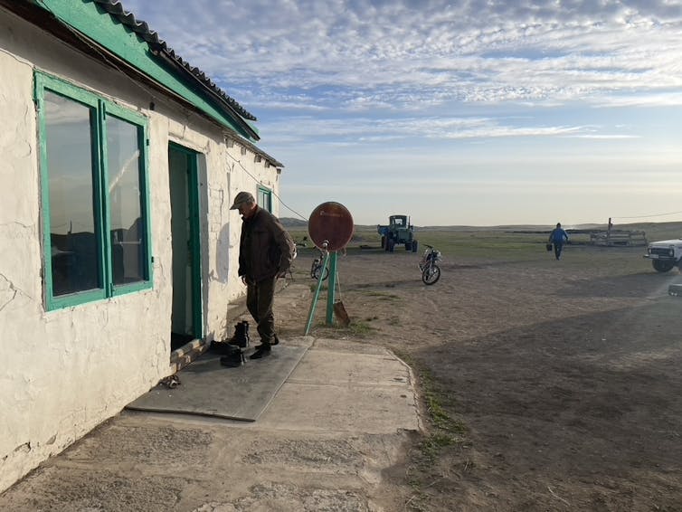 older man approaching door of small house with wide open landscape around it
