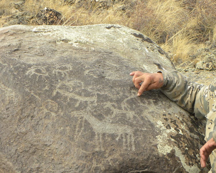 man's arm points to animal silhouettes on a big rock